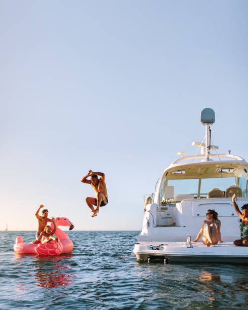 Young people having fun during party on a private boat Young man jumping off the boat in to the sea. Young people having fun during party on a private boat. Men and women on yacht and inflatable toy in sea. jumping into water stock pictures, royalty-free photos & images