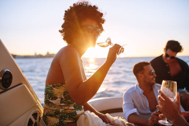 African woman partying with friends in boat African woman drinking during sunset boat party with friends. Group of men and women having a boat party during sunset. drinks on the deck stock pictures, royalty-free photos & images