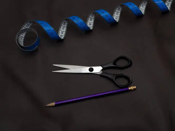 Concept of leather cutting-out. Black scissors, purple pencil and blue twisted tape measure