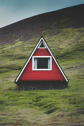 Beautiful view of traditional red A-frame cabin with green meadows and dark moody clouds on a summer day in Iceland