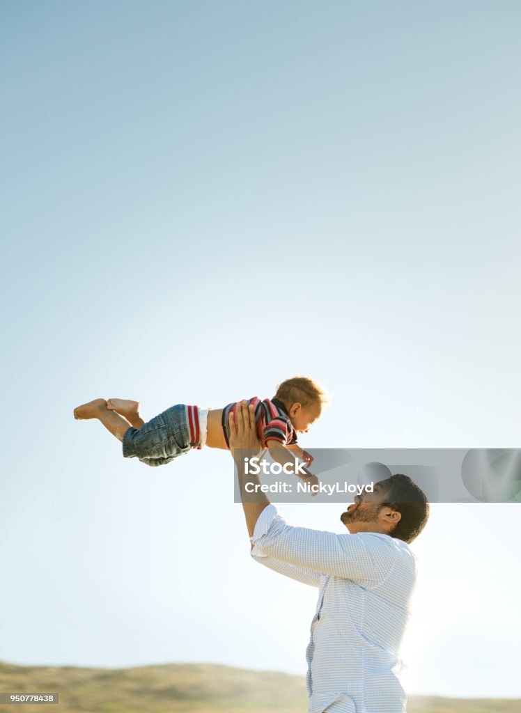 Father and son having fun outdoors Mixed race father throws his adorable son into the air as they laugh and smile at each other Child Stock Photo