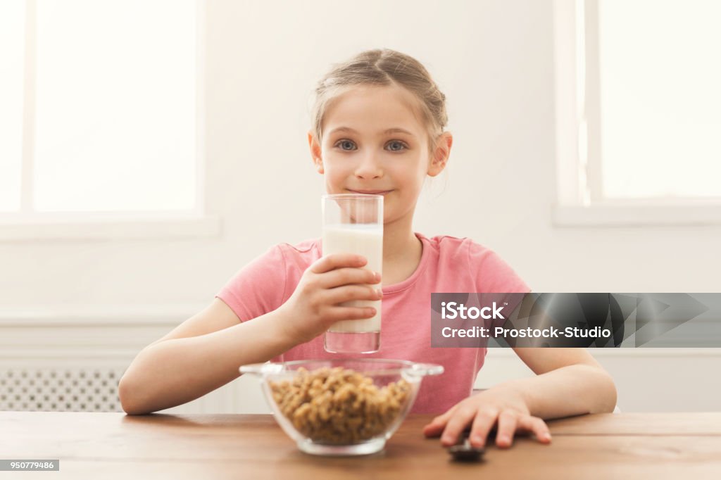 Happy child girl drinking milk Happy child girl drinking milk in glass while sitting at kitchen table. Kid, healthy food, nutrition concept. Beauty Stock Photo