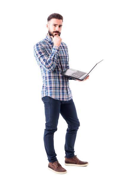 Pensive thoughtful young bearded man with laptop thinking and looking at camera stock photo
