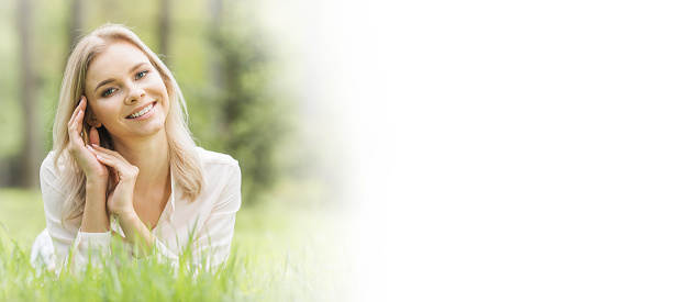Blonde pretty girl laying on the grass in spring park and smiling, white copy space for text