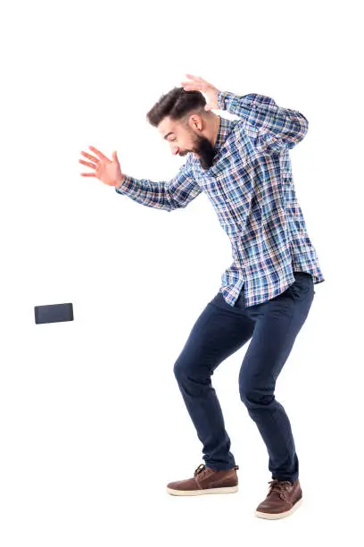 Photo of Shocked sloppy clumsy bearded man dropping mobile phone falling on the ground in mid air