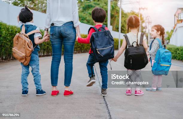 Mother And Pupil And Kids Holding Hands Going To School In First Class With Schoolbag Or Satchel Walking To School Bus Parent And Sonsister Preschool Stock Photo - Download Image Now