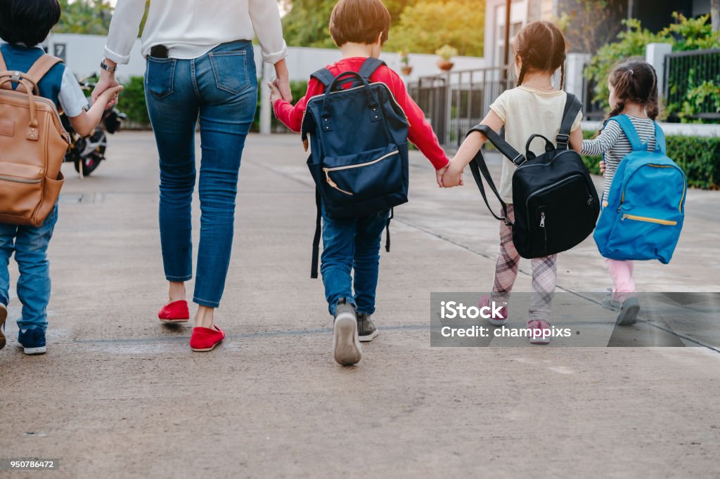 Mother and pupil and kids holding hands going to school in first class with schoolbag or satchel walking to school bus, Parent and son,sister preschool School Building Stock Photo