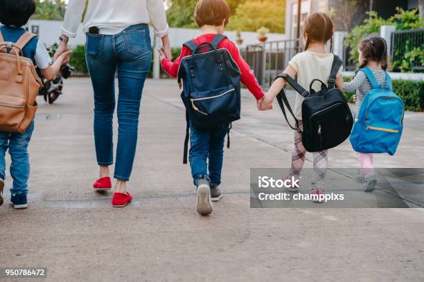 Mother And Pupil And Kids Holding Hands Going To School In First Class With Schoolbag Or Satchel Walking To School Bus Parent And Sonsister Preschool Stock Photo - Download Image Now