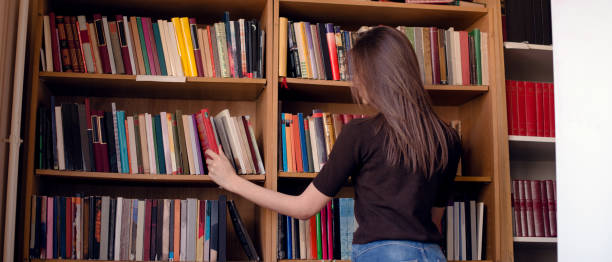 istock Cropped image of woman taking book from bookshelf 950787920