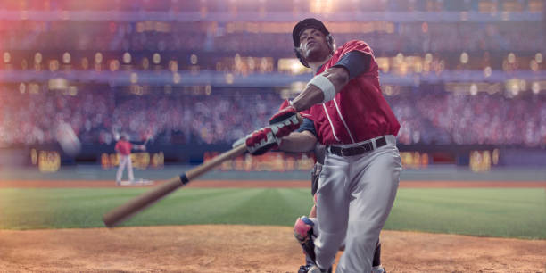 Professional Baseball Batter Hitting Ball During Night Game In Stadium Close up image of a professional male baseball player having just hit the ball. The player is dressed in a generic red and white baseball uniform and wears a black safety helmet. The action takes place in an outdoor baseball stadium full of spectators, with an out of focus background. baseball sport stock pictures, royalty-free photos & images