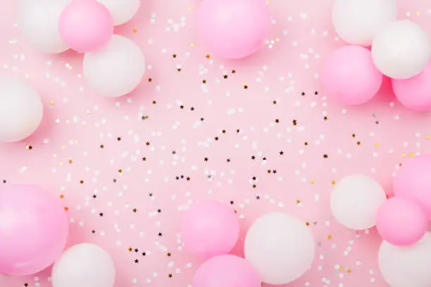 Photo of Pastel pink table with frame from balloons and confetti for birthday top view. Flat lay.