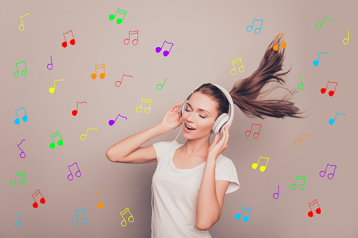 Portrait of happy smiling girl listening music in headphones over background of notes