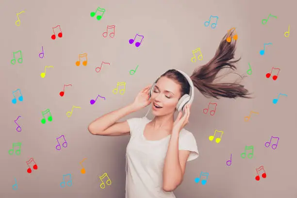 Photo of Portrait of happy smiling girl listening music in headphones over background of notes