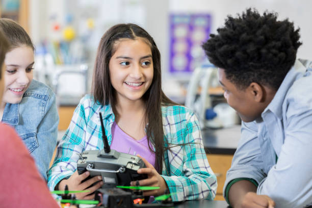 Teenage girl builds a drone with friends during class Confident Hispanic female high school student builds a drone with her friends during an after school engineering club. They are programming the drone. high school high school student science multi ethnic group stock pictures, royalty-free photos & images