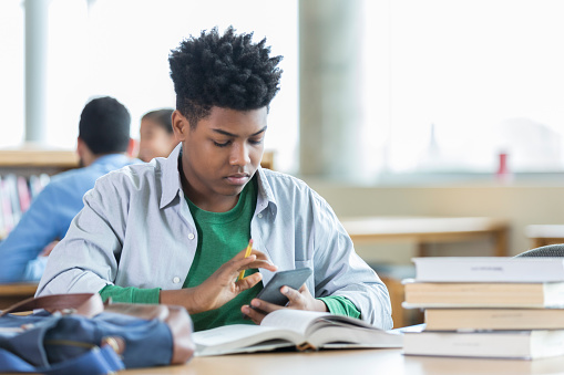 African American high school student studies for an exam while in the campus library.