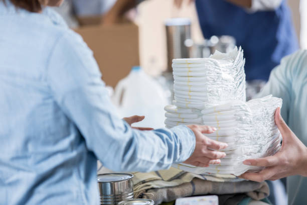 Unrecognizable volunteers organize diapers at local food bank A couple of unrecognizable food bank volunteers pass a stack of diapers to sort along with blankets and canned goods. adult diaper stock pictures, royalty-free photos & images