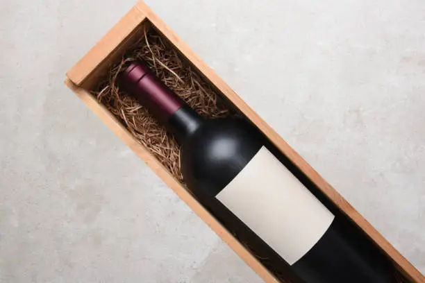 Red Wine Bottle: A single bottle of Cabernet wine in a wood case with packing straw. Bottle is at an angle with copy space on both sides.