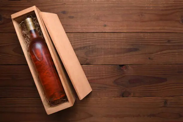 Blush Wine Box: A single Bottle of White Zinfandel wine in its wooden case on a dark wood table with copy space.