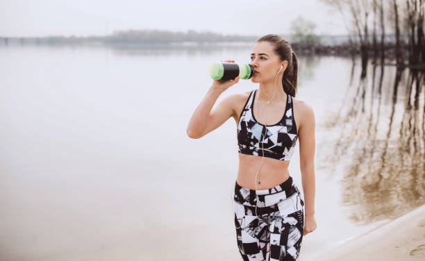 istock Young woman drinking protein shake after morning training outdoors near river 950845936