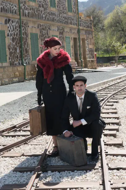 Young couple with vintage suitcase in deep thoughts siting on the trainlines ready for separation and a journey.