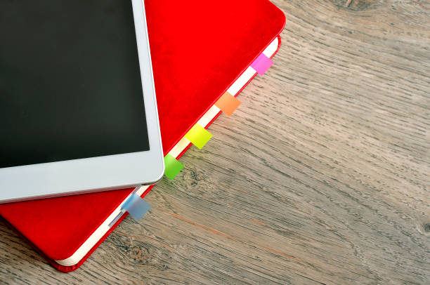 istock Red notebook and white tablet on a table with a wooden texture. 950850686