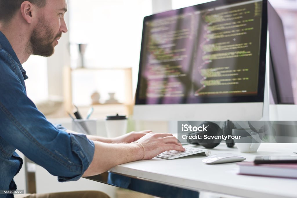 Computer genius at work Serious pensive experienced male programmer typing code on computer while working on new software application in modern comfortable office Computer Programmer Stock Photo