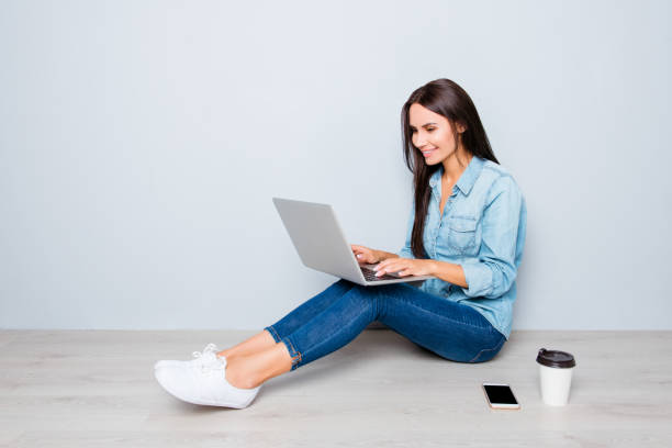 istock Young smiling woman working on laptop while sitting on floor 950854740