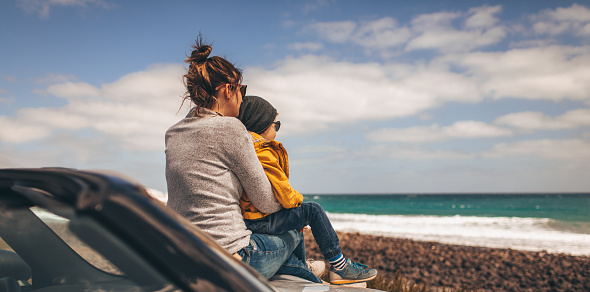 Photo of a little boy and his mother taking a brake and enjoying seaside view while on a road trip with their convertible car // wide photo dimensions