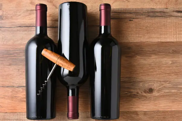 Top view of three red wine bottles on a wood table with an old fashioned corkscrew.