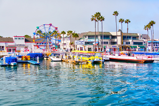 Popular pier at Balboa peninsula in Southern California with ferris wheel, tourist shops, restaurants and boats doting the harbor ferry terminal.