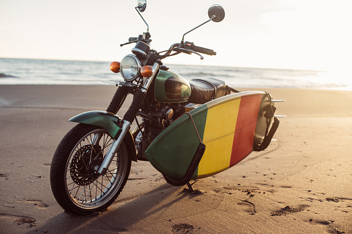 Motorcycle with surfboard parked on tropical beach