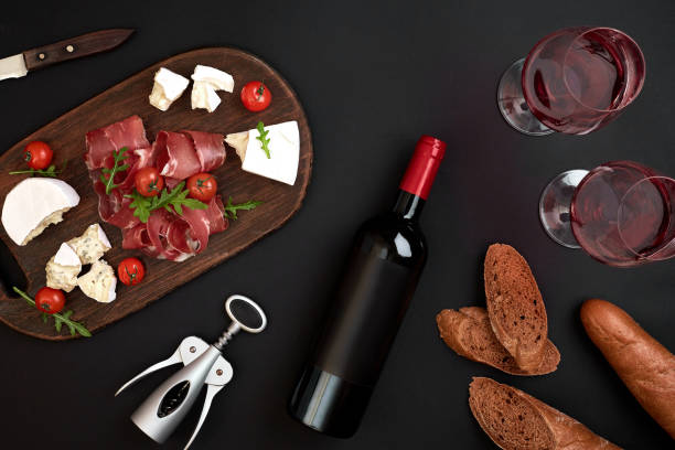 istock Red wine, cheese, cherry tomato, bread and prosciutto on wooden board over black backdrop, top view, copy space 950886718