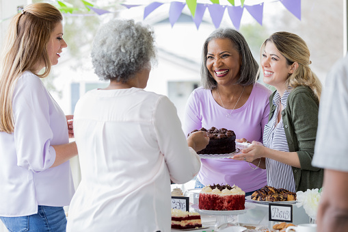 Cheerful female volunteers serve customers during a cancer awareness bake sales.