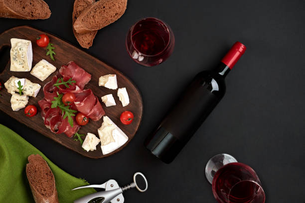 istock Red wine, cheese, cherry tomato, bread and prosciutto on wooden board over black backdrop, top view, copy space 950887480