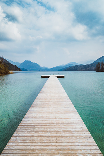 Scenic panorama view of an idyllic wooden landing stage on a beautiful lake in the Alps on a moody cloudy day in summer with retro vintage filter effect