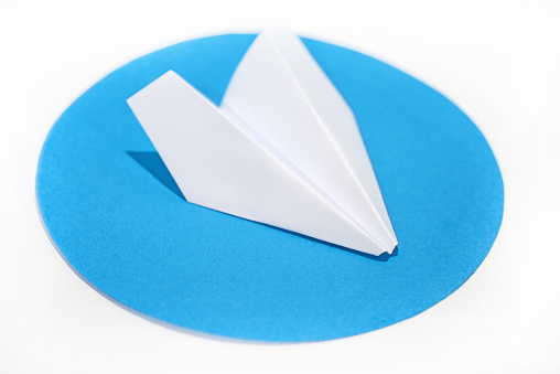 White paper plane on round blue circle. Abstract photo.