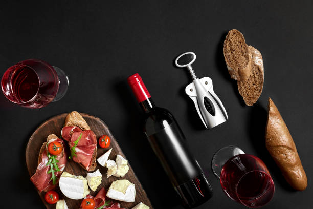 istock Red wine, cheese, cherry tomato, bread and prosciutto on wooden board over black backdrop, top view, copy space 950901164
