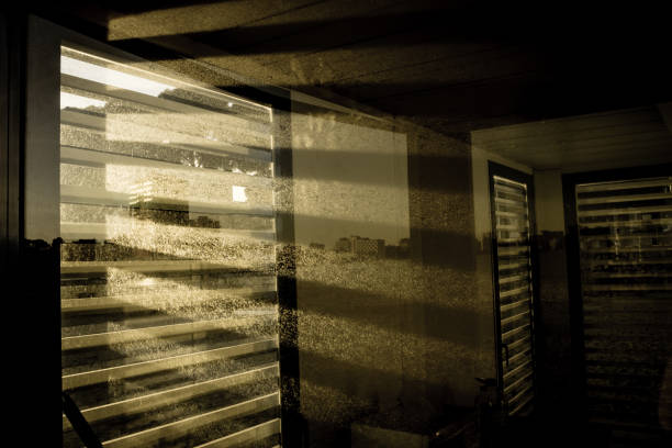 Light streaming through the shuttered windows of an office building.  The beams of light catch the dirt on the windows.  In the distance  the urban skyline is partially visible.  Palma Nova, Calvia, Mallorca.
