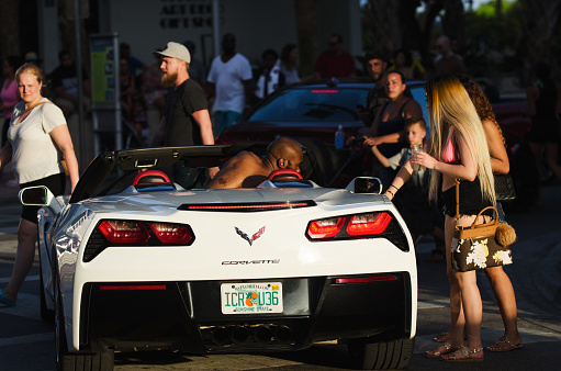 Miami - April 21, 2018: Young women draw attention from onlookers as they take a ride in a white Corvette convertible on Ocean Drive in South Beach.