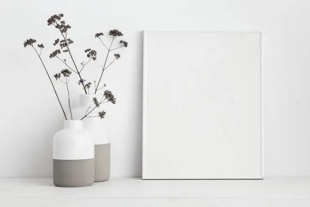 Photo of Mock up white frame and dry twigs in vase on book shelf or desk. White colors.