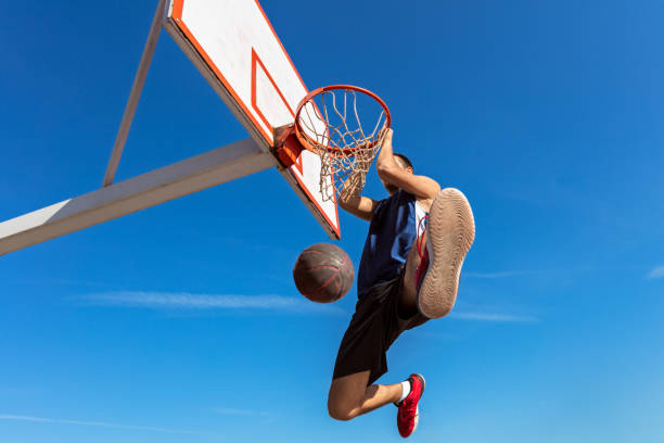 istock Slam Dunk. Side view of young basketball player making slam dunk 950922890