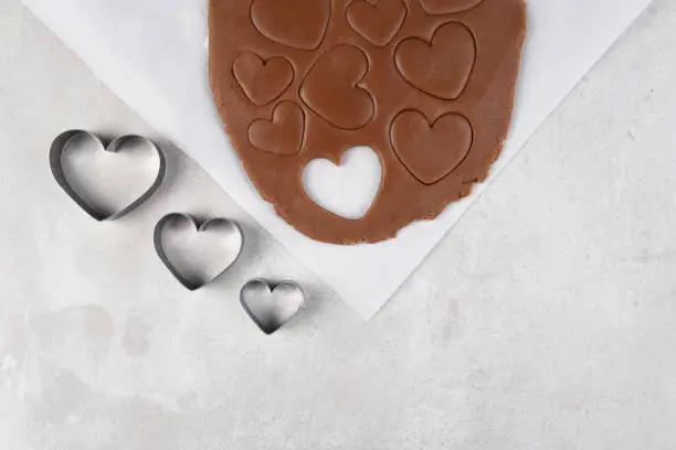 Valentines Day Baking: Three heart shape cookie cutters in a line with a sheet of chocolate cookie dough.