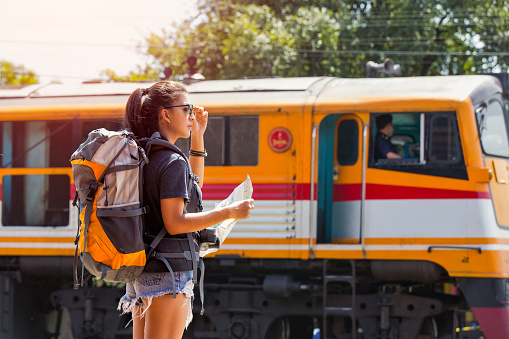 Young asian woman traveler with backpack and sunglass looking the map with train background at Ayutthaya train station.