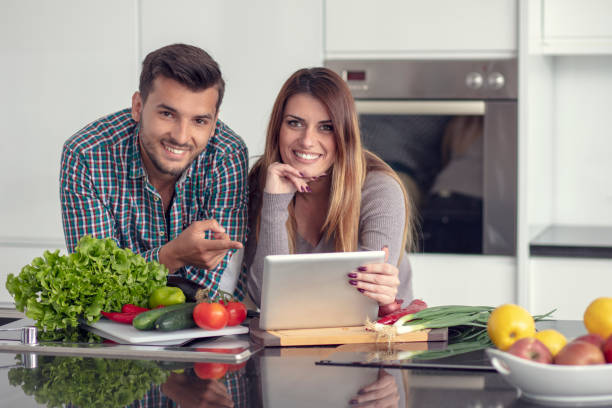 retrato de feliz joven pareja cocinar juntos en la cocina en casa. - standing digital tablet couple love fotografías e imágenes de stock