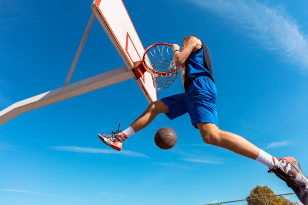 istock Slam Dunk. Side view of young basketball player making slam dunk 950931944