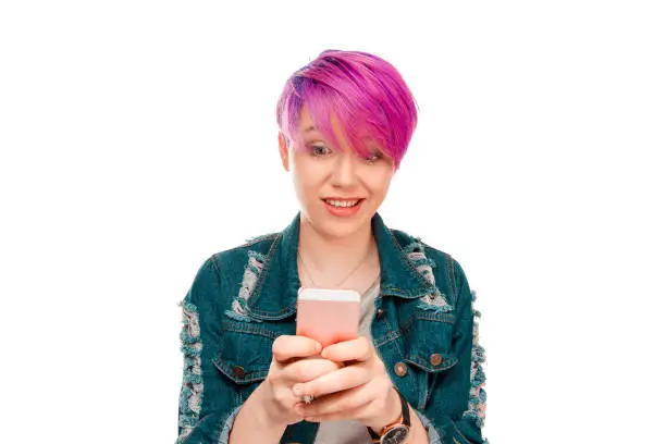 Oh no! Really?! Young astonished magenta short hair woman lady looking at phone standing on the pure white background, reading news at her mobile phone, wearing casual gray shirt, jeans jacket