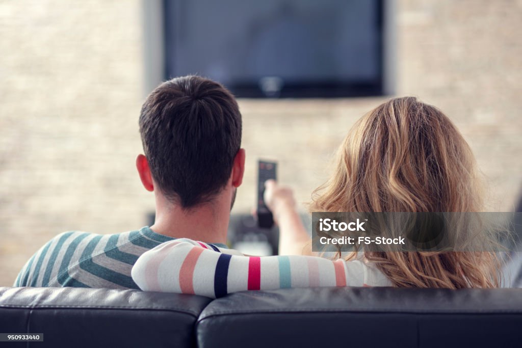 Casal jovem feliz relaxante e assistindo TV em casa. - Foto de stock de Assistir TV royalty-free