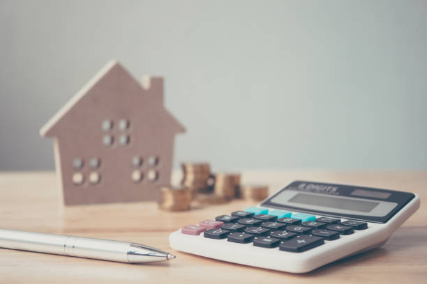A pen and calculator with a mini house and coins on the background
