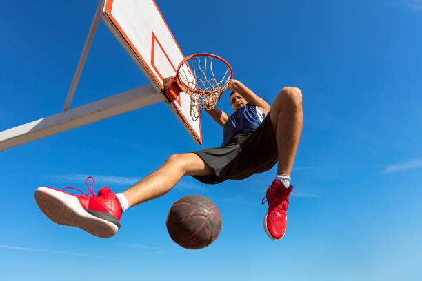 istock Slam Dunk. Side view of young basketball player making slam dunk 950937602