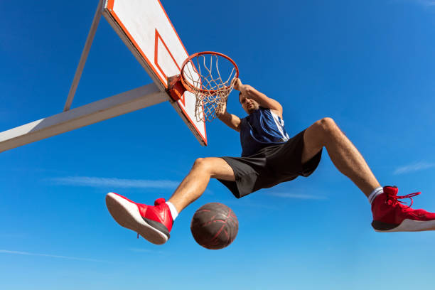 istock Slam Dunk. Side view of young basketball player making slam dunk 950937816